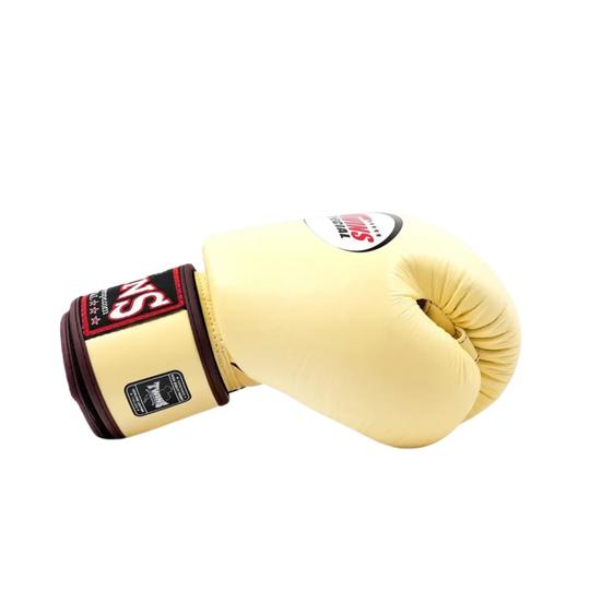 Twins Special Bokshandschoen Vanilla – Zijaanzicht van een premium leren bokshandschoen in elegante vanillekleur met donkerrode polsband en het klassieke Twins-logo. Biedt optimale demping, stevige polsondersteuning en een luxe afwerking voor intensieve bokstraining en sparring. Perfect voor boksers die stijl en prestaties willen combineren.