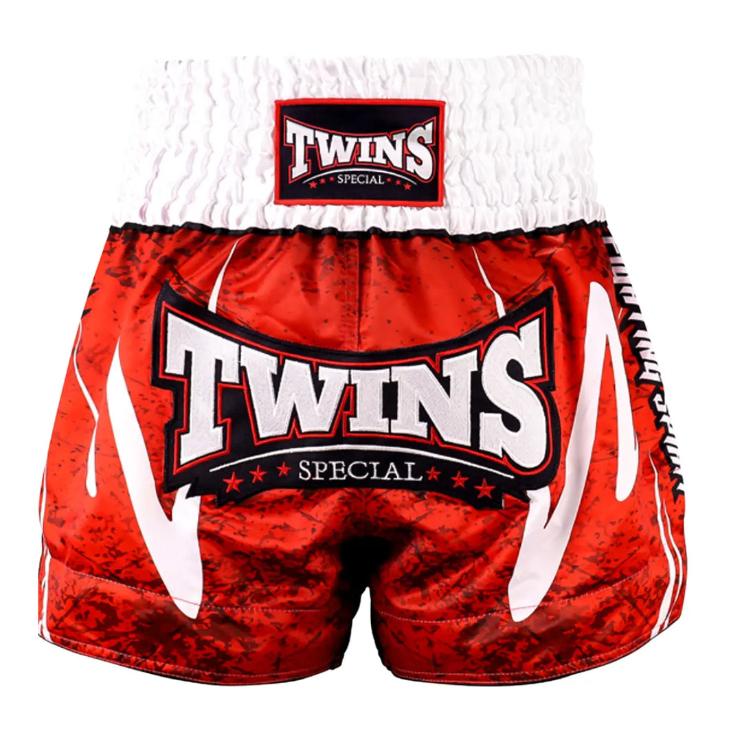 Front view of the Twins Special Muay Thai shorts in red with a white elastic waistband. The shorts feature a large embroidered Twins logo on the front, bold contrast details on the sides, and a traditional Muay Thai cut that offers freedom of movement and a secure fit during training and sparring.