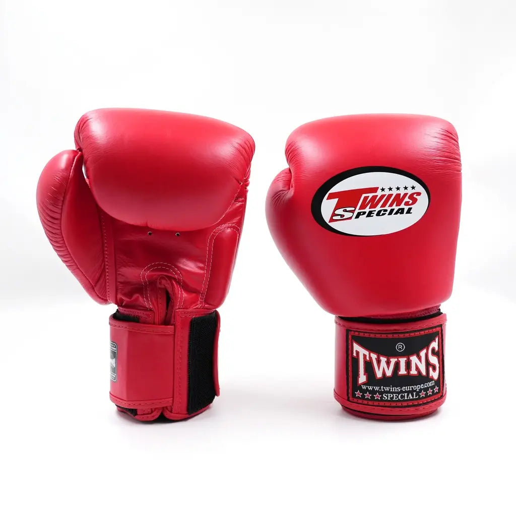 Twee rode Twins bokshandschoenen van leer op witte achtergrond, met wit Twins-logo op de vuistzijde en rood label met merknaam op de polsband.