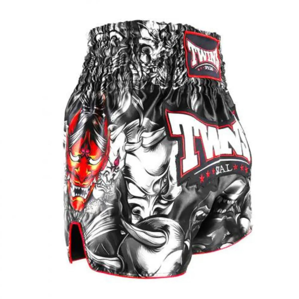 Zijaanzicht van het Twins Special kickboksbroekje met opvallende Japanse Oni-maskerprint in rood en wit op een zwarte basis. De diepe split aan de zijkant biedt extra bewegingsvrijheid tijdens trappen en knieën. Rode biezen langs de randen zorgen voor een extra visuele boost. De broek is gemaakt van satijn polyester en heeft een stevige elastische tailleband met klassieke TWINS-label. Ideaal voor kickboksers die kracht, cultuur en karakter willen uitstralen tijdens hun training.