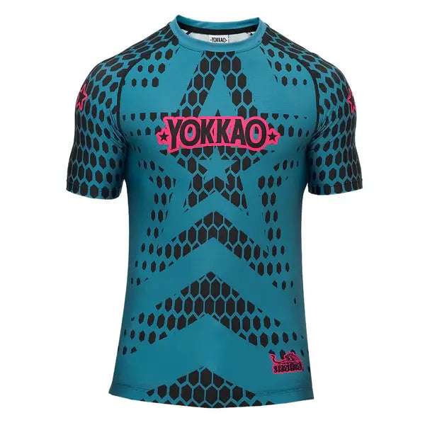Vooraanzicht van het Yokkao compression shirt Stargame in de kleur Ottanium. Het shirt heeft een opvallend turquoise design met zwart honingraatpatroon en een roze Yokkao-logo op de borst. De strakke pasvorm en korte mouwen zorgen voor optimale ondersteuning en bewegingsvrijheid tijdens intensieve trainingen.