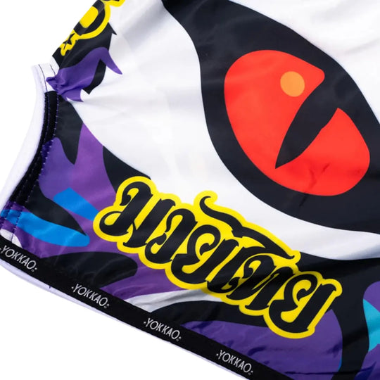 Close-up van het YOKKAO Angry Tiger kickboks broekje met groot kattenoog-design. De kleuren paars, wit en oranje springen sterk naar voren. Het detail benadrukt de unieke Thaise stijl van het short.