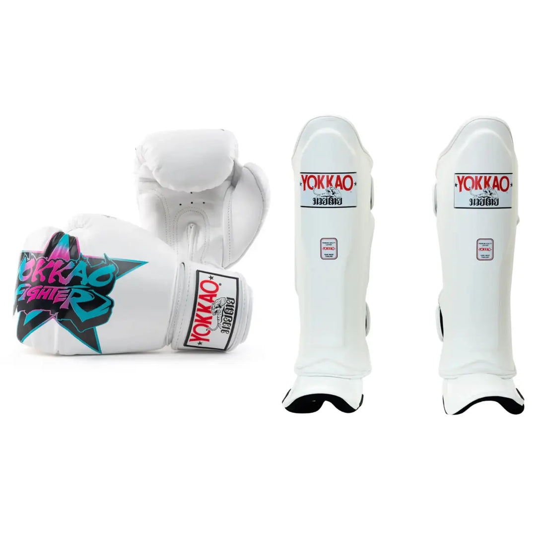 A professional martial arts gear bundle featuring white boxing gloves with a bold black star graphic containing pink and teal "YOKKAO FIGHTER" text. The set includes matching white professional leather shin guards, with all items prominently displaying the white, red, and black YOKKAO brand logo.