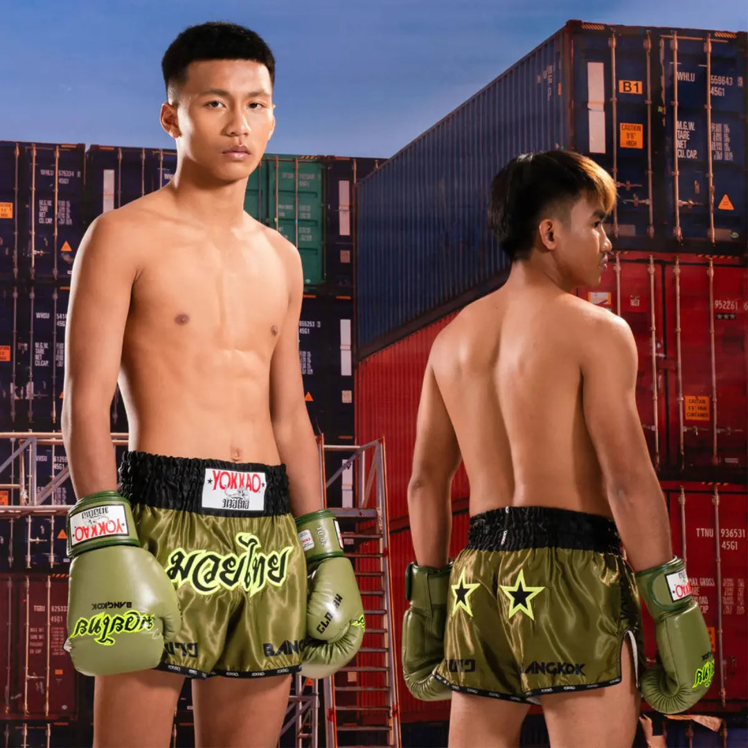 Twee kickboksers dragen de Yokkao Bangkok Bokshandschoenen en Kickboksbroek Groen. De combinatie van legergroen satijn en neongele details straalt kracht en stijl uit, perfect voor vechters die trainen met focus en klasse.
