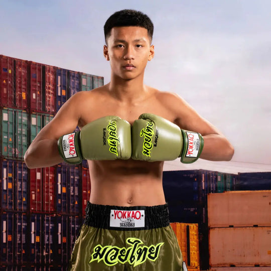 Kickbokser met Yokkao Bokshandschoenen Bangkok Groen poseert met een krachtige houding. De handschoenen en short tonen het iconische Yokkao-design in legergroen met neongele accenten, symbool voor kracht, focus en Thaise vakmanschap.