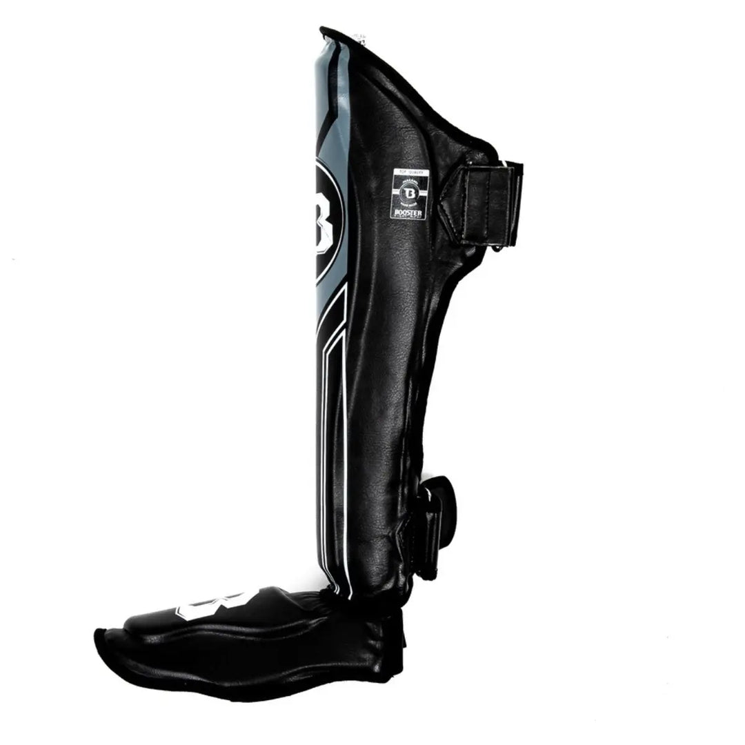 Zijaanzicht van een Booster BGL V9 scheenbeschermer in de kleur zwart met donkergrijze accenten. De afbeelding toont de been- en voetbescherming met de klittenbandsluitingen