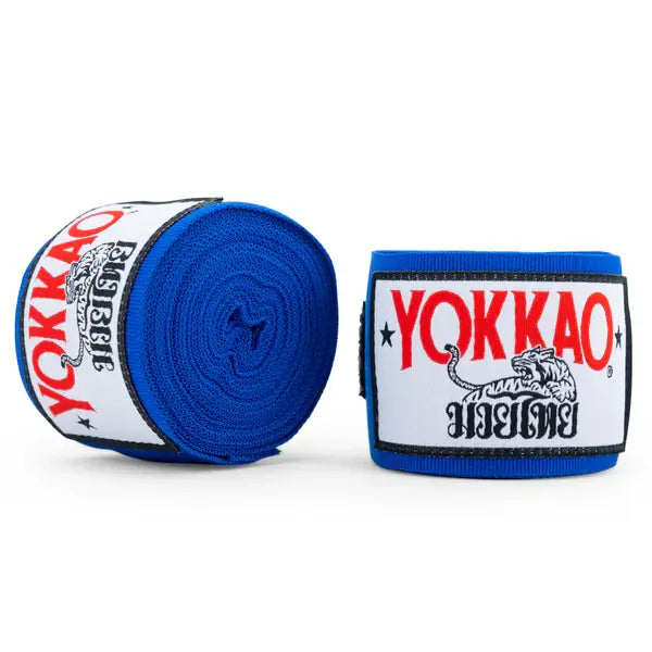 Set blauwe Yokkao handwraps tegen een witte achtergrond, waarbij één bandage is opgerold en de andere gesloten met klittenbandsluiting. De witte logo patch met rood YOKKAO-logo en zwarte details is duidelijk zichtbaar. Geschikt voor bokstraining, kickboksen en Muay Thai ter ondersteuning van polsen en knokkels.