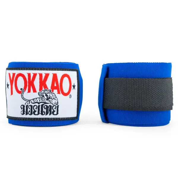 Blauwe Yokkao handwraps tegen een witte achtergrond met zicht op zowel de voorkant als de achterkant. Aan de voorkant is de witte patch met rood YOKKAO-logo en zwarte details zichtbaar, terwijl de achterkant de zwarte klittenbandsluiting toont. Geschikt voor stevige pols- en knokkelondersteuning tijdens boksen en kickboksen.