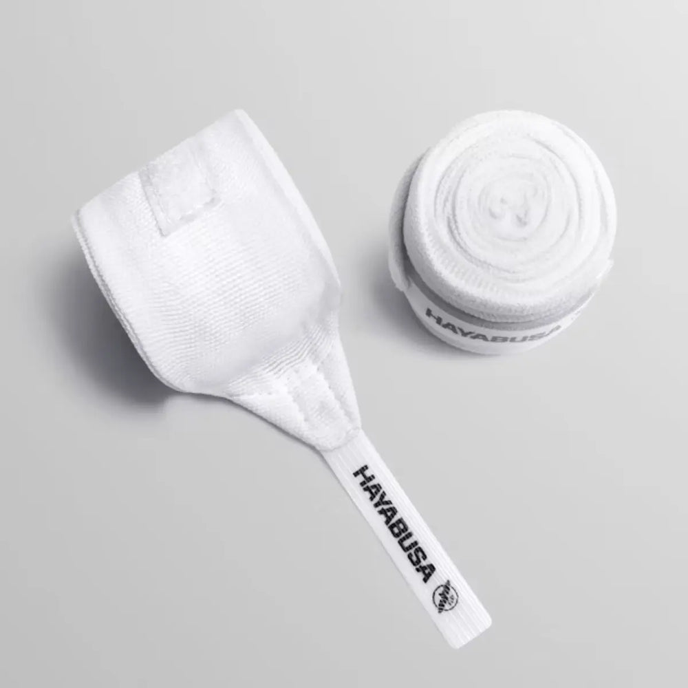 Top-down productfoto van een opgerolde witte Hayabusa handbandage en de onopgerolde duimlus met het zwarte Hayabusa logo op een grijze ondergrond