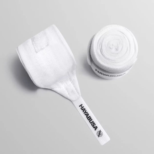 Top-down productfoto van een opgerolde witte Hayabusa handbandage en de onopgerolde duimlus met het zwarte Hayabusa logo op een grijze ondergrond