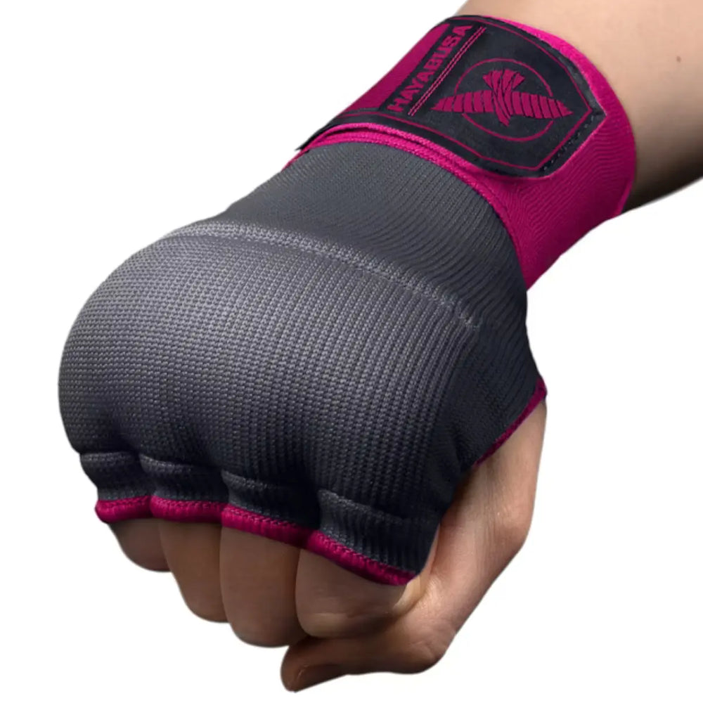 Close-up van een gebalde vuist die de grijze, vingerloze Hayabusa binnenhandschoen draagt, vastgezet met de felroze polsband met het Hayabusa logo.
