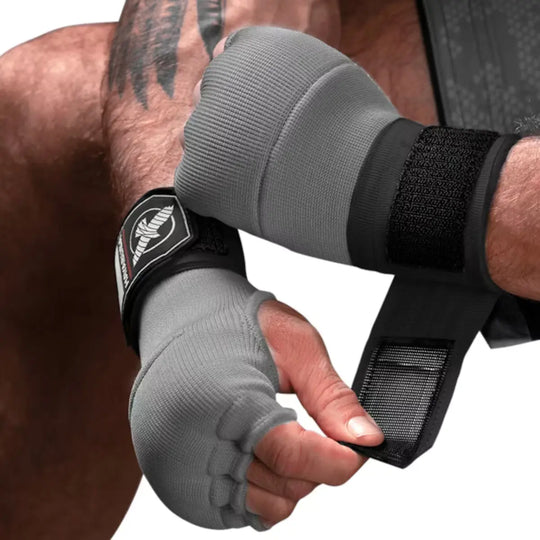 Close-up van een man met getatoeëerde armen die grijze Hayabusa binnenhandschoenen (quick wraps) draagt en de zwarte klittenbandsluiting op de pols vastmaakt.