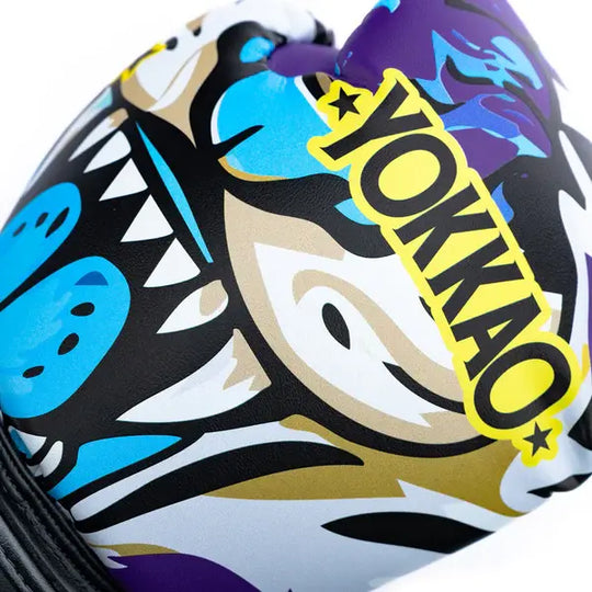 Close-up van Yokkao Angry Tiger bokshandschoen met opvallende gele YOKKAO-logo op paarse achtergrond. De handschoen toont een kleurrijke tijgerprint met blauwe en witte accenten en scherpe grafische details. Het ontwerp combineert zwart, paars en turquoise voor een krachtige uitstraling.