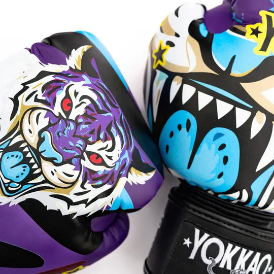 Close-up van paarse Yokkao bokshandschoenen met opvallende Angry Tiger print in paars, blauw en wit. De handschoenen tonen een agressieve tijgerillustratie met rode ogen en grafische details op een zwarte basis. Het Yokkao-logo is zichtbaar op de polssluiting.