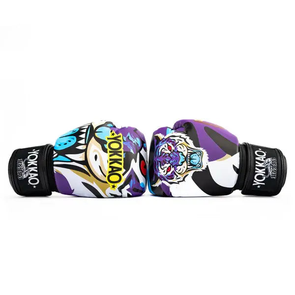 Twee Yokkao Angry Tiger bokshandschoenen liggend tegenover elkaar tegen een witte achtergrond. De paarse handschoenen tonen de kleurrijke tijgerprint met blauwe en witte accenten en het gele YOKKAO-logo op de voorkant. De zwarte klittenbandsluiting met merklogo is zichtbaar aan beide zijden.