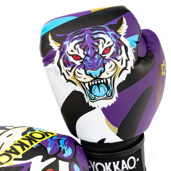 Close-up van Yokkao Angry Tiger bokshandschoen met grote tijgerillustratie op de voorzijde. Het design combineert paars, zwart en wit met blauwe accenten en opvallende rode ogen. Onderaan is de zwarte klittenbandsluiting met Yokkao-logo zichtbaar.