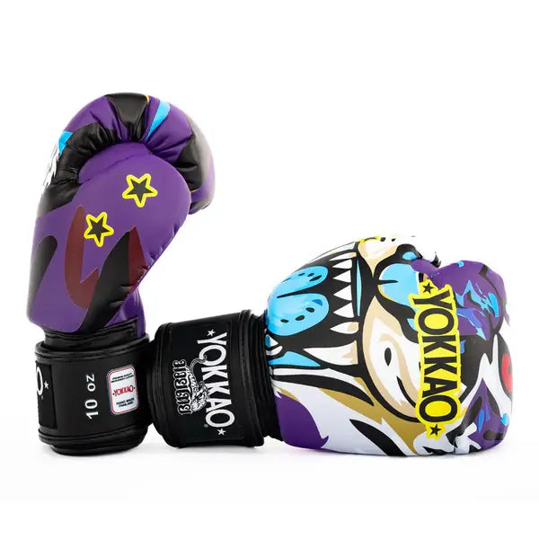 Twee Yokkao Angry Tiger bokshandschoenen in paars met opvallende tijgerprint, gefotografeerd tegen een witte achtergrond. Eén handschoen ligt horizontaal met zichtbaar geel YOKKAO-logo, de andere staat rechtop met 10 oz label op de zwarte klittenbandsluiting. Het design combineert paars, zwart, wit en blauwe accenten met speelse sterdetails.
