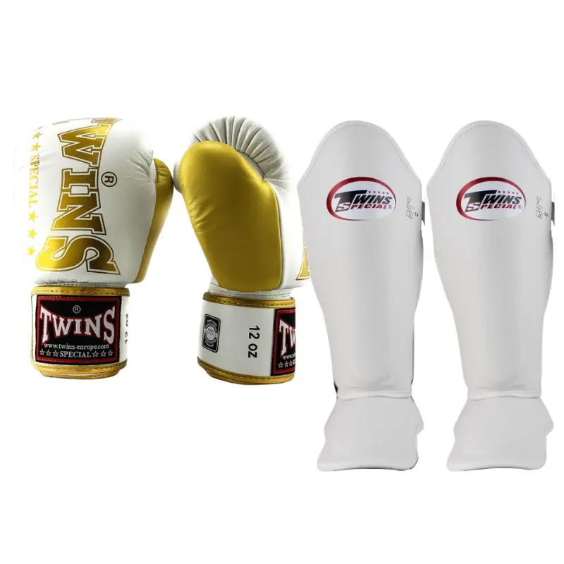  Twins Special kickboksset BGVL-8 in de kleur wit met metallic goud. De set bestaat uit een paar bokshandschoenen (12oz) en een paar bijpassende scheenbeschermers met rode en zwarte Twins logo's.