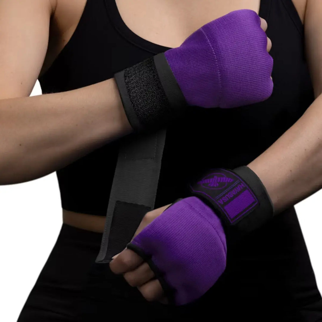 Close-up van een vrouw in een zwarte sporttop die de paarse Hayabusa binnenhandschoenen (quick wraps) draagt en de lange zwarte polsbandage met klittenband vastmaakt.
