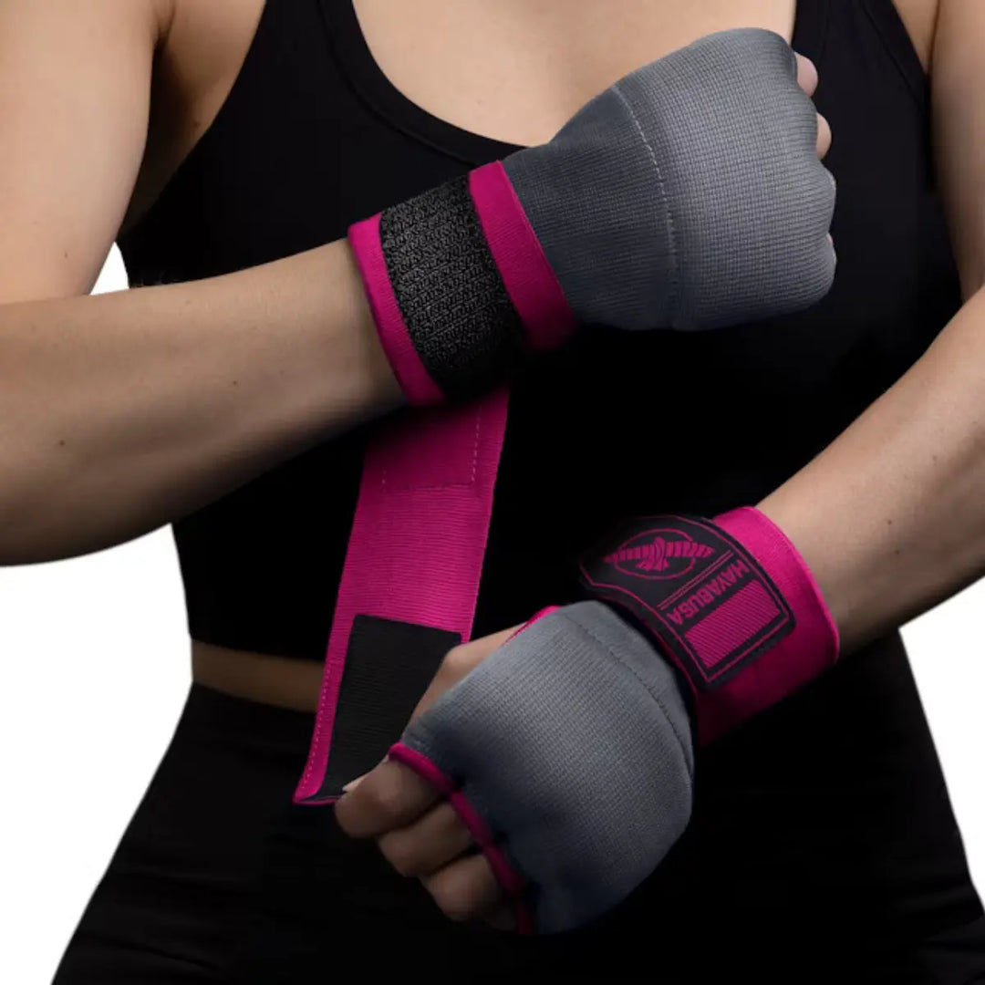 Close-up van een vrouw in een zwarte sporttop die de Hayabusa binnenhandschoenen (quick wraps) in de kleuren grijs en felroze draagt en de klittenbandsluiting vastmaakt.
