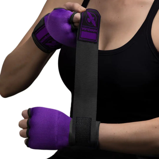 Een vrouw in een zwarte sporttop wikkelt haar hand in met de paarse Hayabusa binnenhandschoen en lange zwarte polsbandage, waarbij het logo op de manchet duidelijk zichtbaar is.
