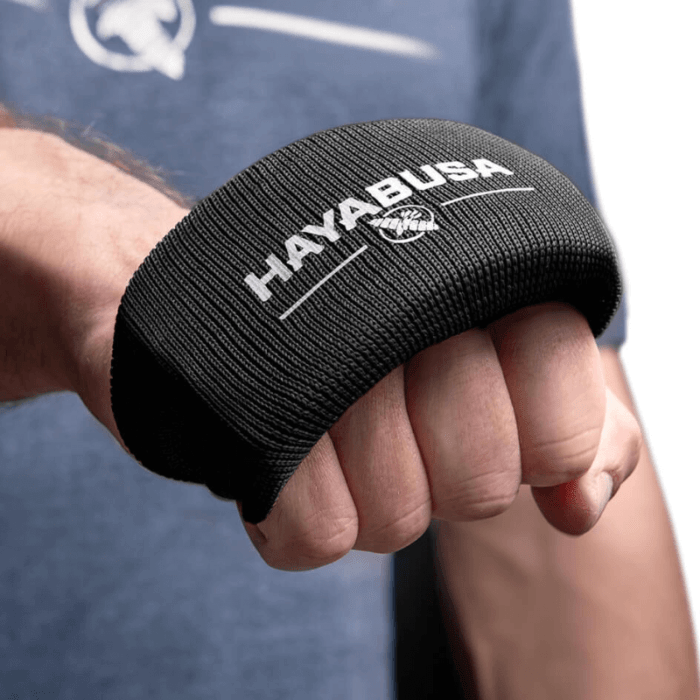 Een zwarte Hayabusa Boxing Knuckle Guard gedragen om de knokkels van een gebalde vuist, met het Hayabusa-logo en adelaarsembleem in wit bovenop.