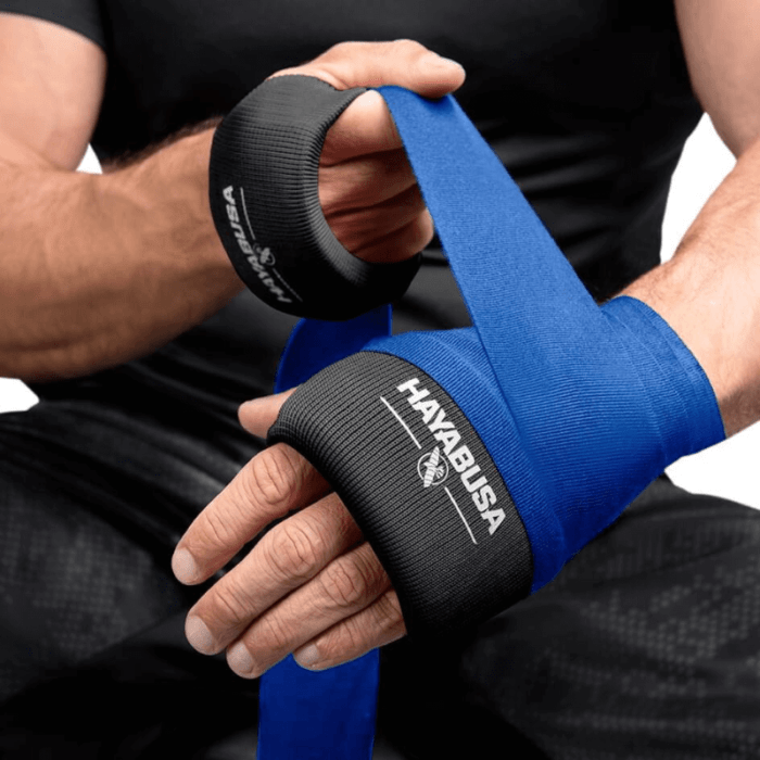 Een persoon wikkelt een blauwe boksband om de pols met een zwarte Hayabusa Boxing Knuckle Guard zichtbaar op de andere hand.