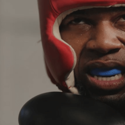 Een bokser draagt een hoofdbeschermer en handschoenen, geconcentreerd en klaar voor een training of gevecht.