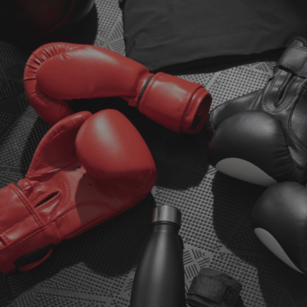 Een verzameling van rode en zwarte bokshandschoenen, sportkleding en fitnessaccessoires netjes weergegeven op een gestructureerde achtergrond.