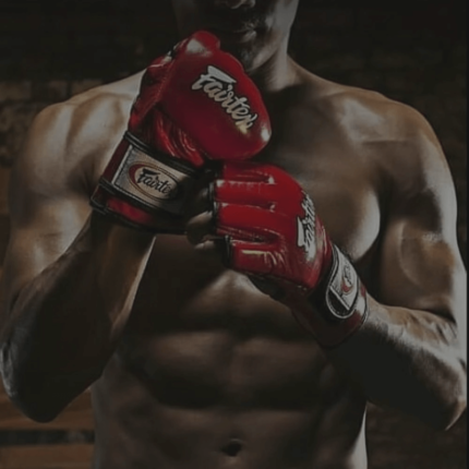 Een gespierde vechtsporter met gekruiste rode bokshandschoenen voor de borst in een donkere omgeving.