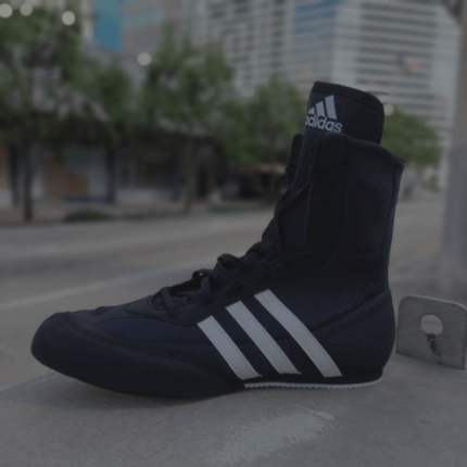 Een zwart-witte boksschoen van het merk Adidas staat op een stedelijke stoep.