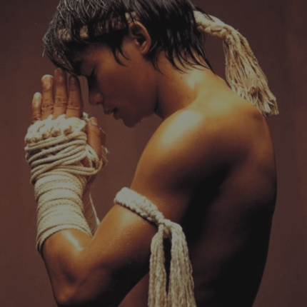 Een vechtsporter in traditionele gevechtsuitrusting mediteert met touw gewikkelde handen voor het gezicht.