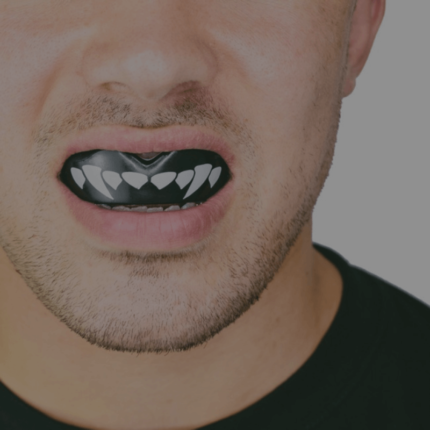 Close-up van een persoon met een zwarte gebitsbeschermer in de mond, waarop een patroon lijkt dat lijkt op witte tanden of vlammen.