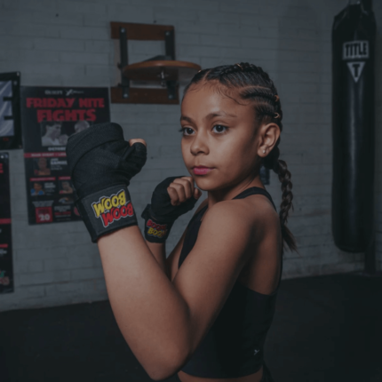 Een jong meisje in een gevechtshouding met bokshandschoenen aan, klaar om te sparren.
