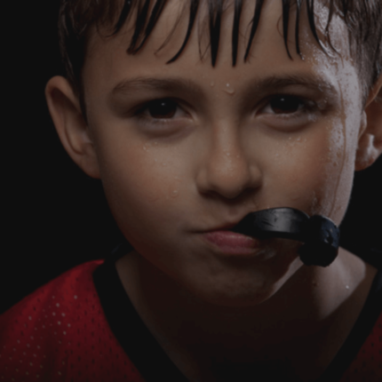 Een jonge jongen met een vochtige huid en een mondbeschermer, kijkt ernstig naar de camera.