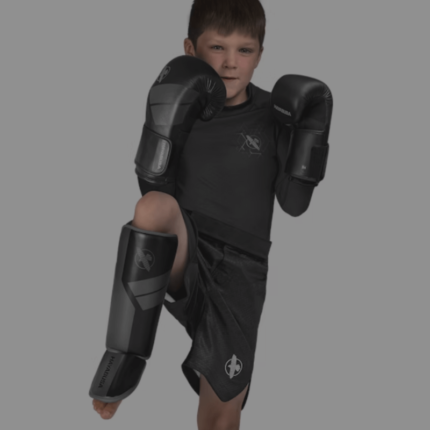 Een jongen in een vechthouding draagt bokshandschoenen en scheenbeschermers, klaar voor training.