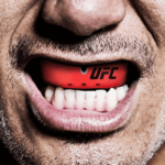 Close-up van een persoon die een rode Opro UFC mondbeschermer draagt, die goed zichtbaar is tegen een glimlach.