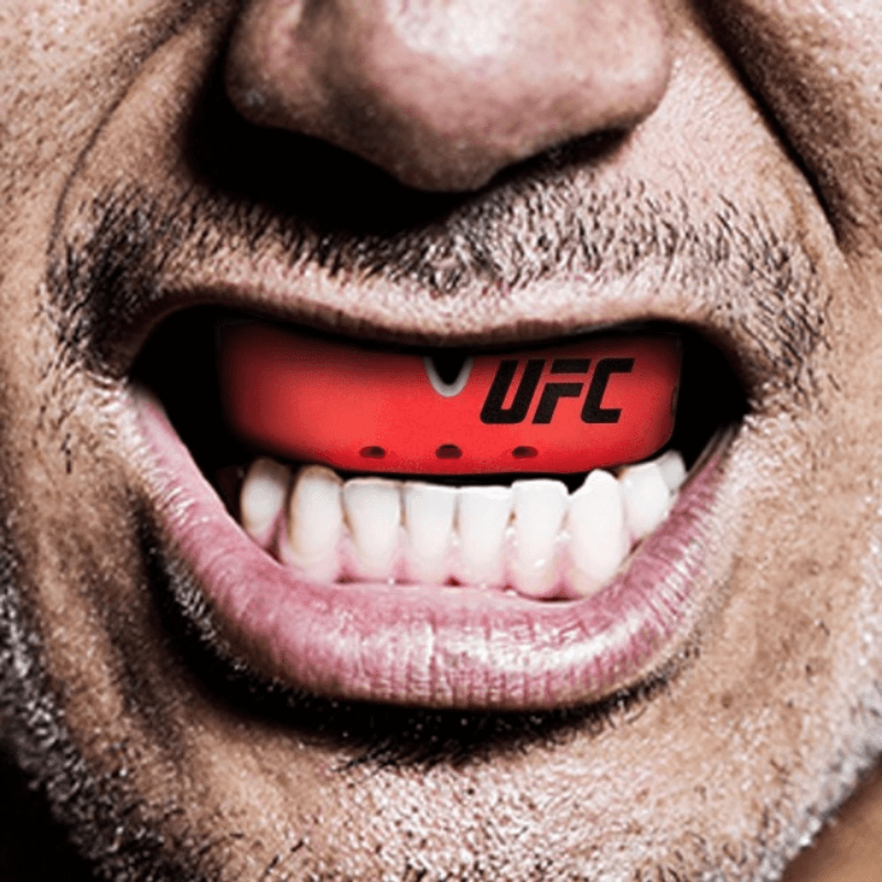 Close-up van een persoon die een rode Opro UFC mondbeschermer draagt, die goed zichtbaar is tegen een glimlach.