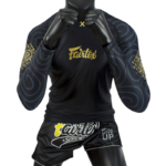 Fairtex vechtsportoutfit bestaande uit een zwarte rashguard met gouden patronen en zwarte shorts met een gele tekstprint.